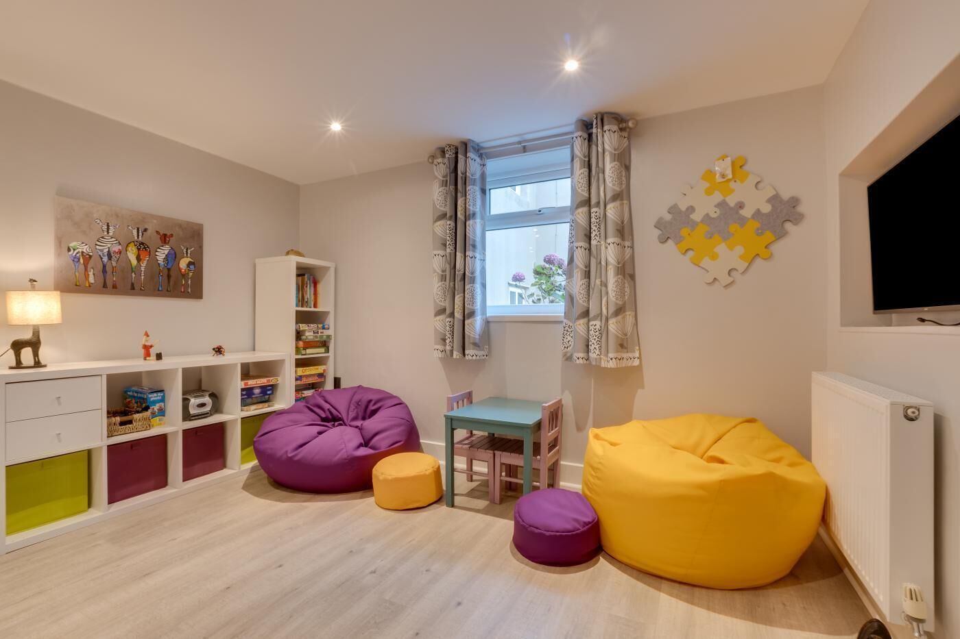 A children's playroom with a bookshelf, bean bags, a table, and a TV.