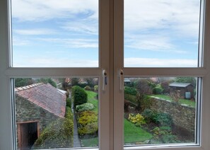 Blick durch ein Fenster auf eine Steinmauer, einen Weg und einen Garten.