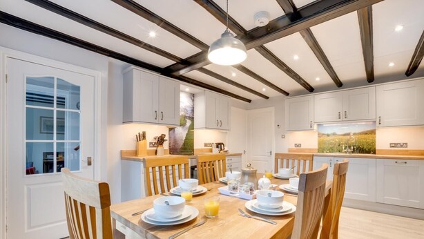 Een moderne keuken met witte kasten, een houten eettafel en een hanglamp.