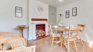Een eetruimte met een ronde tafel, stoelen, een open haard en een klok aan de muur.