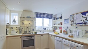 A kitchen with white cabinets, a stove, an oven, a dishwasher, and a washing machine. There is a window with a blue checkered valance, and a bulletin board with papers and notes. - 3 Bed in Walberswick (oc-aaferr) (Walberswick)