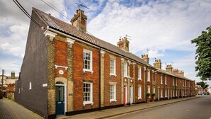 Filas de casas adosadas con fachada de ladrillo, puerta azul y placa con el año visible.