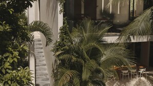 Ein Innenhof mit Treppe, Palmen und einem Essbereich mit Stühlen und Tischen.