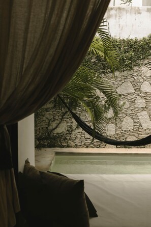 A room with a bed, a stone wall, and a view of a pool. - 16Tulum | Luxury 8BR Villa w/ Pool & Concierge (Tulum)