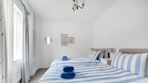 Camera d'albergo con due letti, un'ampia finestra, un lampadario e uno specchio appeso al muro.