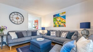 Ein modernes Wohnzimmer mit einem grauen Ecksofa, einem runden Couchtisch und einer großen Wanduhr.