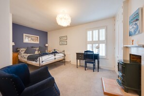 A bedroom with a bed, a desk, a chair, a blue armchair, a fireplace, and a window with blinds. - 3 Bed in Southwold (oc-aafish) (Southwold)