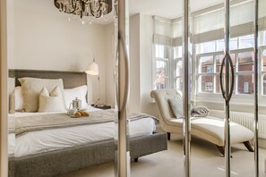 A modern hotel room with a large bed, a sitting area, and large windows offering a view of the city. - 4 Bed in Southwold (oc-aalavh) (Southwold)