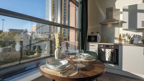 Une cuisine moderne avec une grande fenêtre, une table à manger dressée pour deux personnes et une vue sur le paysage urbain.