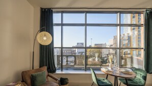 Un salon moderne doté d’une grande fenêtre, d’un canapé, d’une petite table et d’un coin repas avec des chaises.