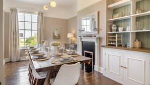 A dining room with a long wooden table set for six, a fireplace, and a bookshelf with decorative items. - 5 Bed in Southwold (oc-aa3cen) (Southwold)