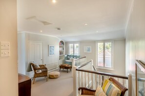Un loft spacieux avec un plafond haut, un escalier, un coin salon avec un canapé et un fauteuil, et une bibliothèque.