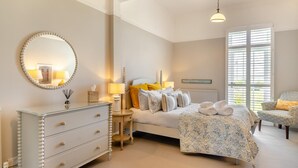 A bedroom with a bed, bedside tables, a dresser, a mirror, and a window with blinds. - 5 Bed in Southwold (oc-aa3cen) (Southwold)