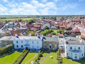 A large, white building with a symmetrical facade, surrounded by a well-maintained lawn and a small garden area. - 5 Bed in Southwold (oc-aa3cen) (Southwold)
