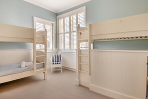 Une chambre avec des lits superposés, une chaise et une fenêtre avec des volets.