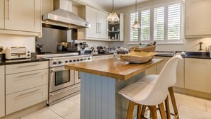 A modern kitchen with a central island, stainless steel appliances, and a large window providing natural light. - 5 Bed in Southwold (oc-aa3cen) (Southwold)