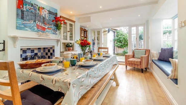 Un coin repas avec une longue table dressée pour le petit-déjeuner, un tableau accroché au-dessus de la table et une vue sur le jardin par la fenêtre.