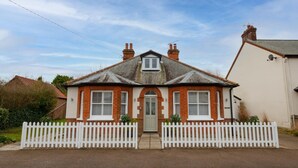 Une maison à deux étages avec une clôture blanche en piquets, une porte d’entrée et un petit jardin.
