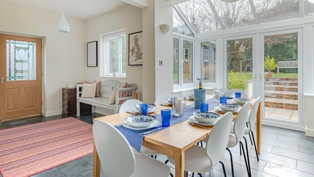 Un coin repas avec une table en bois dressée pour quatre personnes, des chaises blanches et une porte vitrée donnant sur un jardin.