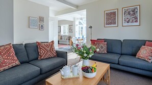 Un salon moderne avec deux canapés gris, une table basse sur laquelle se trouve un panier de fruits, et des œuvres d’art encadrées accrochées aux murs.