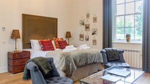 A bedroom with a large bed, two bedside tables, a chair, a glass coffee table, and a window with curtains. - 1 Bed in Wells-next-the-Sea (oc-1939) (Wells-next-the-Sea)