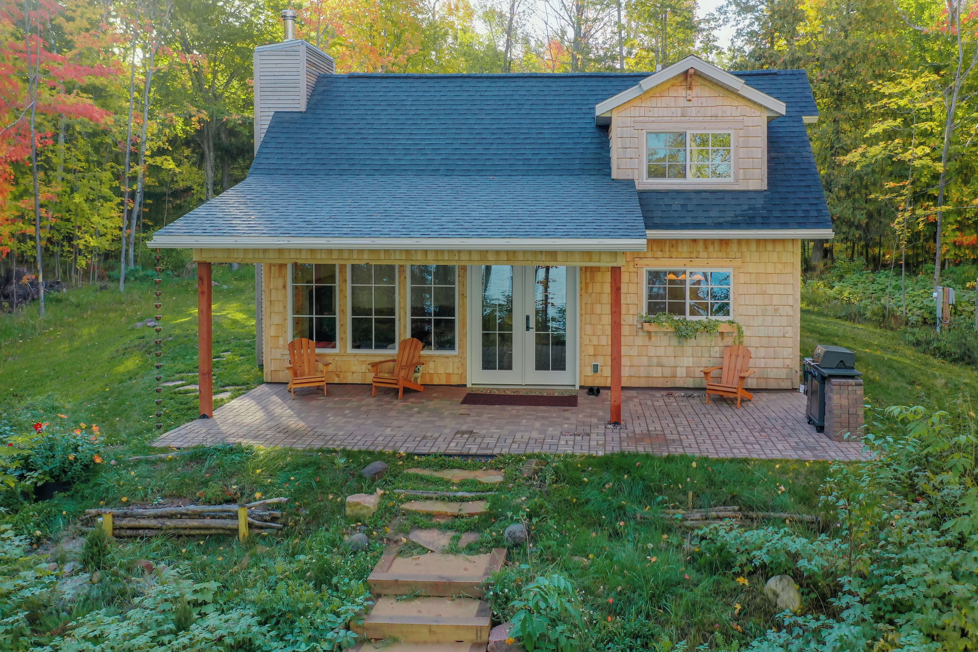 A two-story wooden house with a covered patio, large windows, and a chimney.
