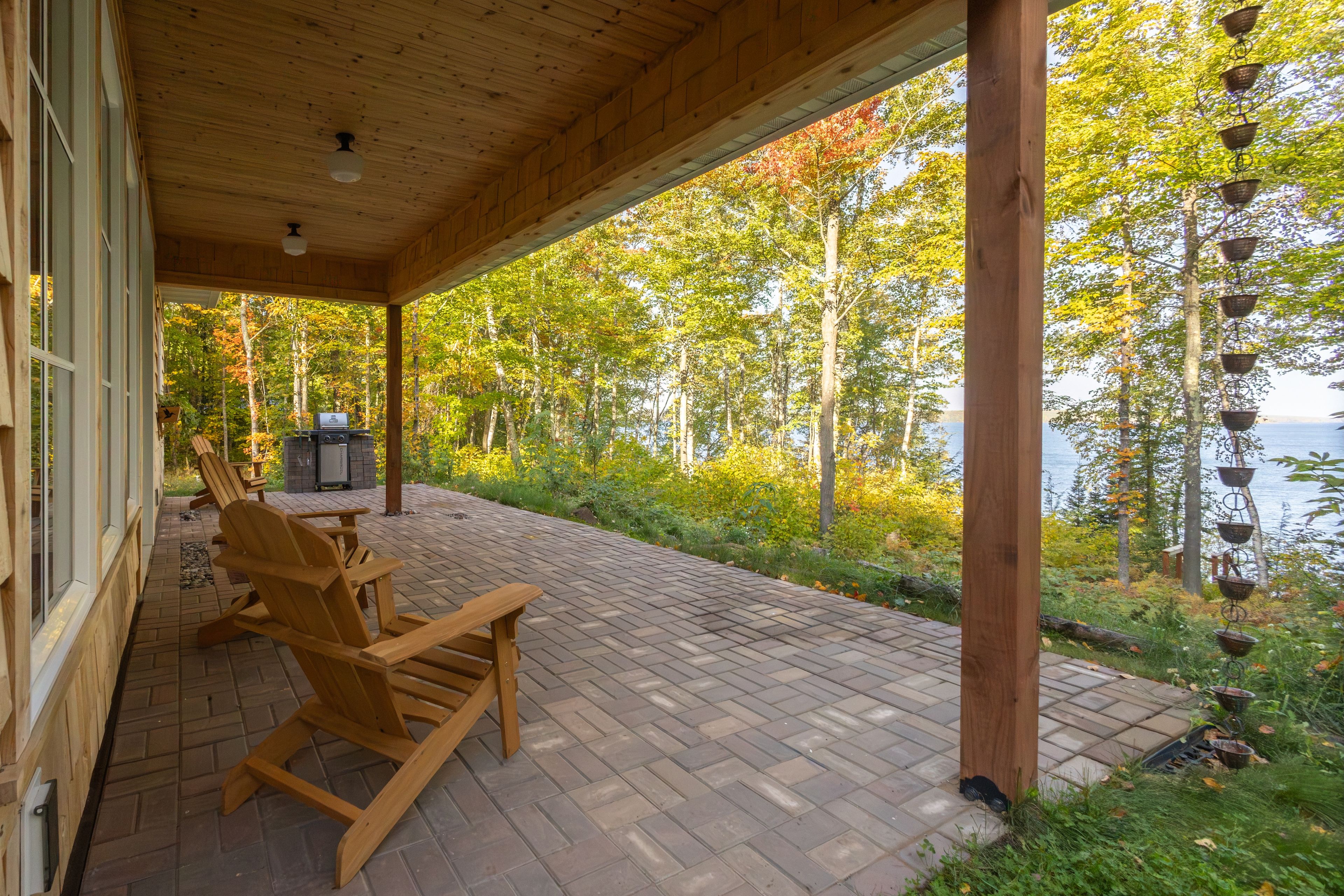 Una terraza de madera con sillas Adirondack, una parrilla y vistas a un lago rodeado de árboles.