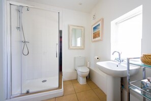 Un baño con cabina de ducha de vidrio, inodoro, lavabo con espejo y un cuadro en la pared.
