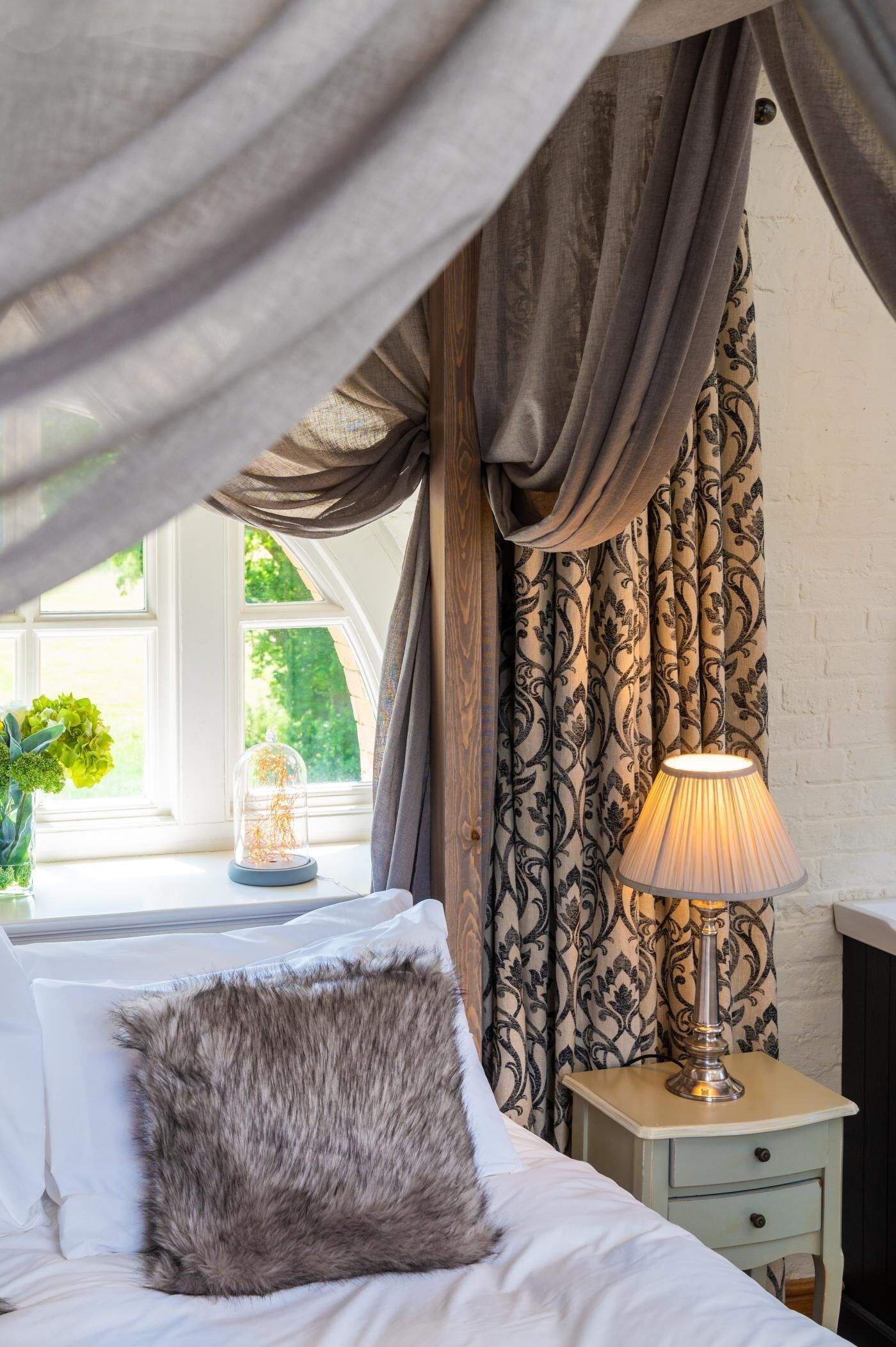 Ein Schlafzimmer mit einem Bett, einem Nachttisch mit Lampe und einem Fenster mit Vorhängen.