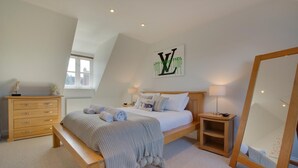 Une chambre à coucher comprenant un lit, une commode en bois, des tables de chevet, un miroir et une œuvre d’art accrochée au mur.