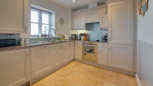 Une cuisine moderne avec des meubles blancs, un plan de travail en granit, un four encastré et une fenêtre équipée de stores.