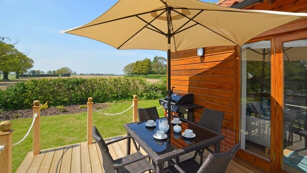 A wooden deck with a table and chairs, a barbecue grill, and a large umbrella providing shade. - 2 Bed in Ingworth (oc-1731) (Ingworth)