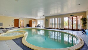 An indoor swimming pool with a separate hot tub area, a seating area with a table and chairs, and large windows with blinds. - 2 Bed in Ingworth (oc-1731) (Ingworth)