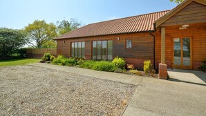 A single-story building with a tiled roof, a gravel driveway, and a small garden area with shrubs and a brick pillar. - 2 Bed in Ingworth (oc-1731) (Ingworth)
