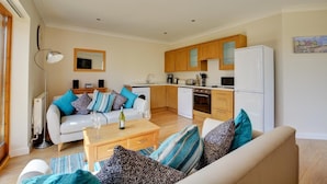 A compact living space with a sofa, coffee table, and a dining area with a kitchen in the background. - 2 Bed in Ingworth (oc-1731) (Ingworth)