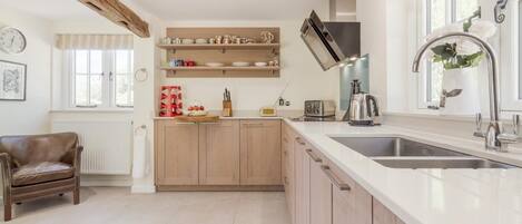 A modern kitchen with wooden cabinets, a built-in oven, a sink, and a chair.