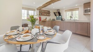 Eine moderne Küche mit Holzschränken, einem für das Frühstück gedeckten Esstisch und einem großen Fenster.