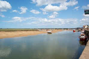 A calm river with boats docked on the right, a sandy shore on the left, and a clear sky above. - 3 Bed in Wells-next-the-Sea (oc-1963) (Wells-next-the-Sea)