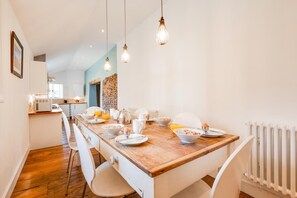 A modern kitchen with a wooden dining table, white chairs, and hanging light fixtures. - 3 Bed in Wells-next-the-Sea (oc-1963) (Wells-next-the-Sea)