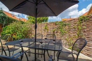 An outdoor patio with a table and chairs, a large umbrella, and a wall covered in climbing plants. - 3 Bed in Wells-next-the-Sea (oc-1963) (Wells-next-the-Sea)