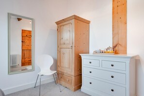 A bedroom with a wooden wardrobe, a white dresser, a white chair, and a mirror on the wall. - 3 Bed in Wells-next-the-Sea (oc-1963) (Wells-next-the-Sea)