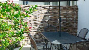 Eine Terrassenausstattung mit Tisch und Stühlen, einer gewobenen Wand und einem Blumentopf.