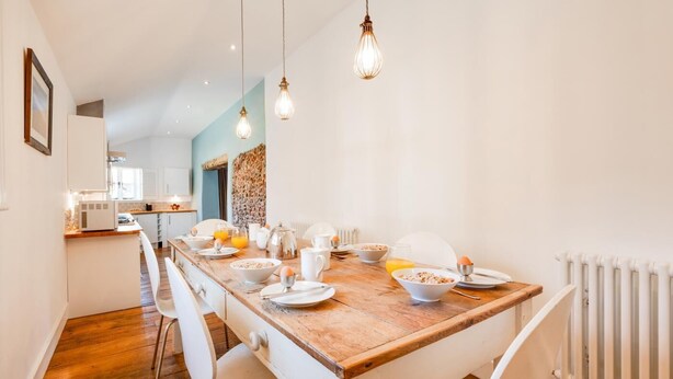 Eine moderne Küche mit einem Holztisch, weißen Stühlen und Pendelleuchten.
