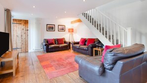 Ein geräumiges Wohnzimmer mit Holzboden, zwei Ledersofas mit roten Kissen, einer Stehlampe und einer Treppe.