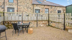A stone building with a gravel patio, a table with chairs, and a grill. - 1 Bed in Powburn (oc-nb662) (Ilderton)