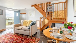 A cozy living room with a sofa, a dining table set for two, a wooden staircase, and a view of the outdoors. - 1 Bed in Powburn (oc-nb662) (Ilderton)
