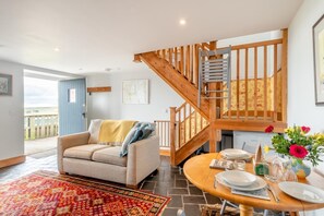 A cozy living room with a sofa, a dining table set for two, a wooden staircase, and a view of the outdoors. - 1 Bed in Powburn (oc-nb662) (Ilderton)