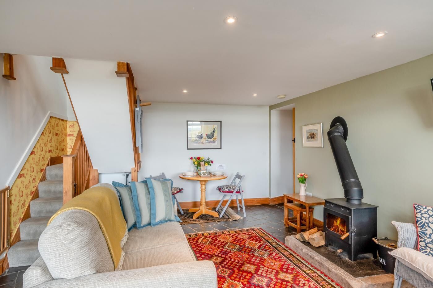A cozy living room with a sofa, a table, a fireplace, a staircase, and a painting on the wall.