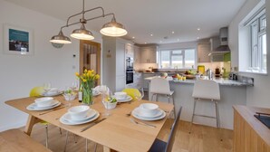 A modern kitchen with white cabinets, a central island, and a dining area with yellow chairs and a wooden table set for six. - 3 Bed in St. Merryn (oc-p00725) (Saint Merryn)