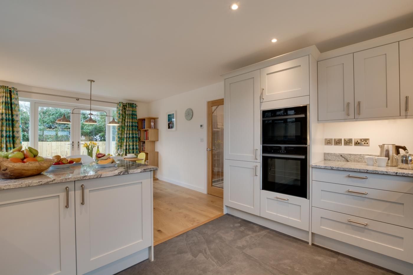 A modern kitchen with white cabinetry, a double oven, and a granite countertop.
